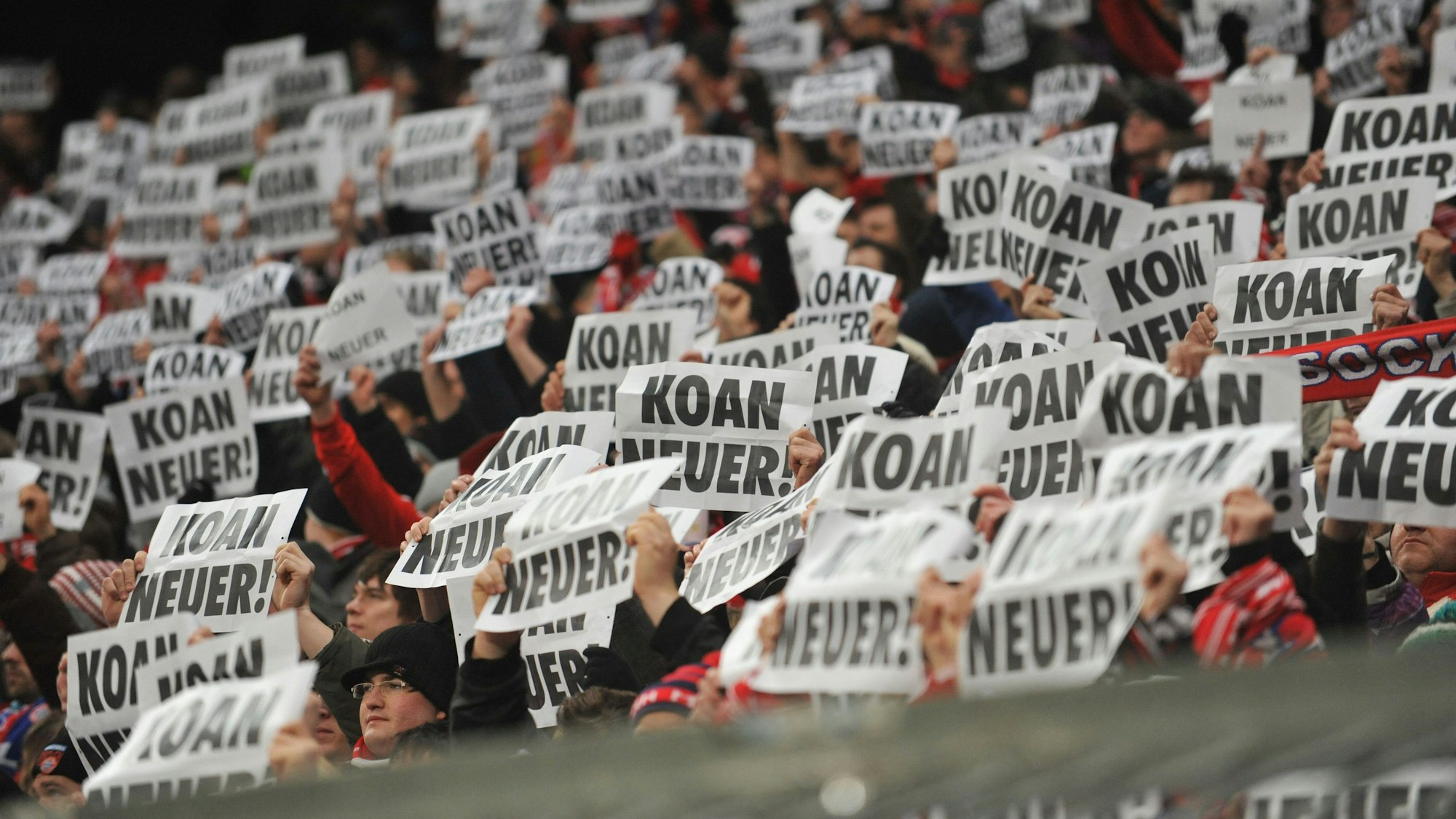 Fans von Bayern München halten Plakate mit der Aufschrift „KOAN NEUER!“ hoch.
