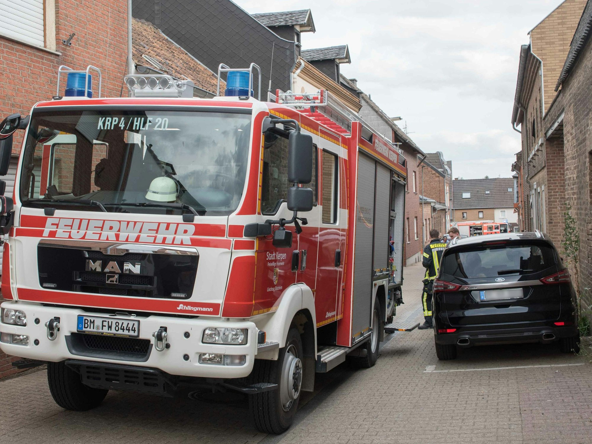 Einsatzkräfte der Feuerwehr stehen in einer Straße mit Einfamilienhäusern in Kerpen.