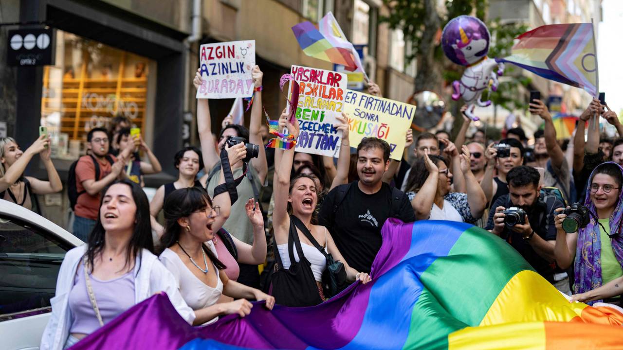 Menschen protestieren mit Schildern und einer großen Regenbogenflagge gegen die LGBTQ-feindliche Politik in der Türkei.
