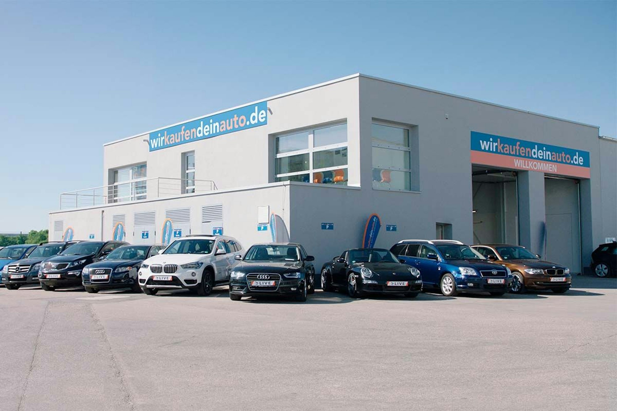 wirkaufendeinauto.de Filiale mit geparkten Gebrauchtwagen davor.