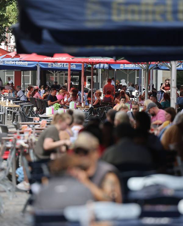 Menschen sitzen in Lokalen im Außenbereich unter Sonnenschirmen. Ab diesem Jahr gelten neue, verbindliche Regeln für die Außengastronomie. Lokale in der Altstadt und im Bereich der Deutzer Messe müssen die Vorgaben ab dem 1. Oktober umsetzen.