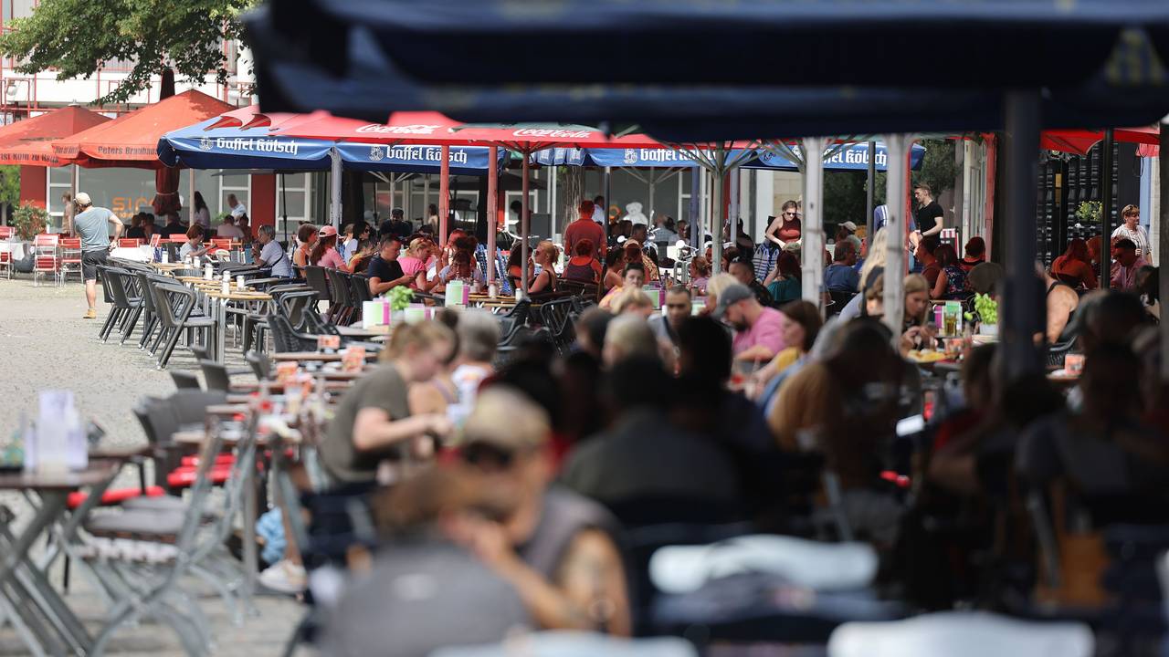 Menschen sitzen in Lokalen im Außenbereich unter Sonnenschirmen. Ab diesem Jahr gelten neue, verbindliche Regeln für die Außengastronomie. Lokale in der Altstadt und im Bereich der Deutzer Messe müssen die Vorgaben ab dem 1. Oktober umsetzen.