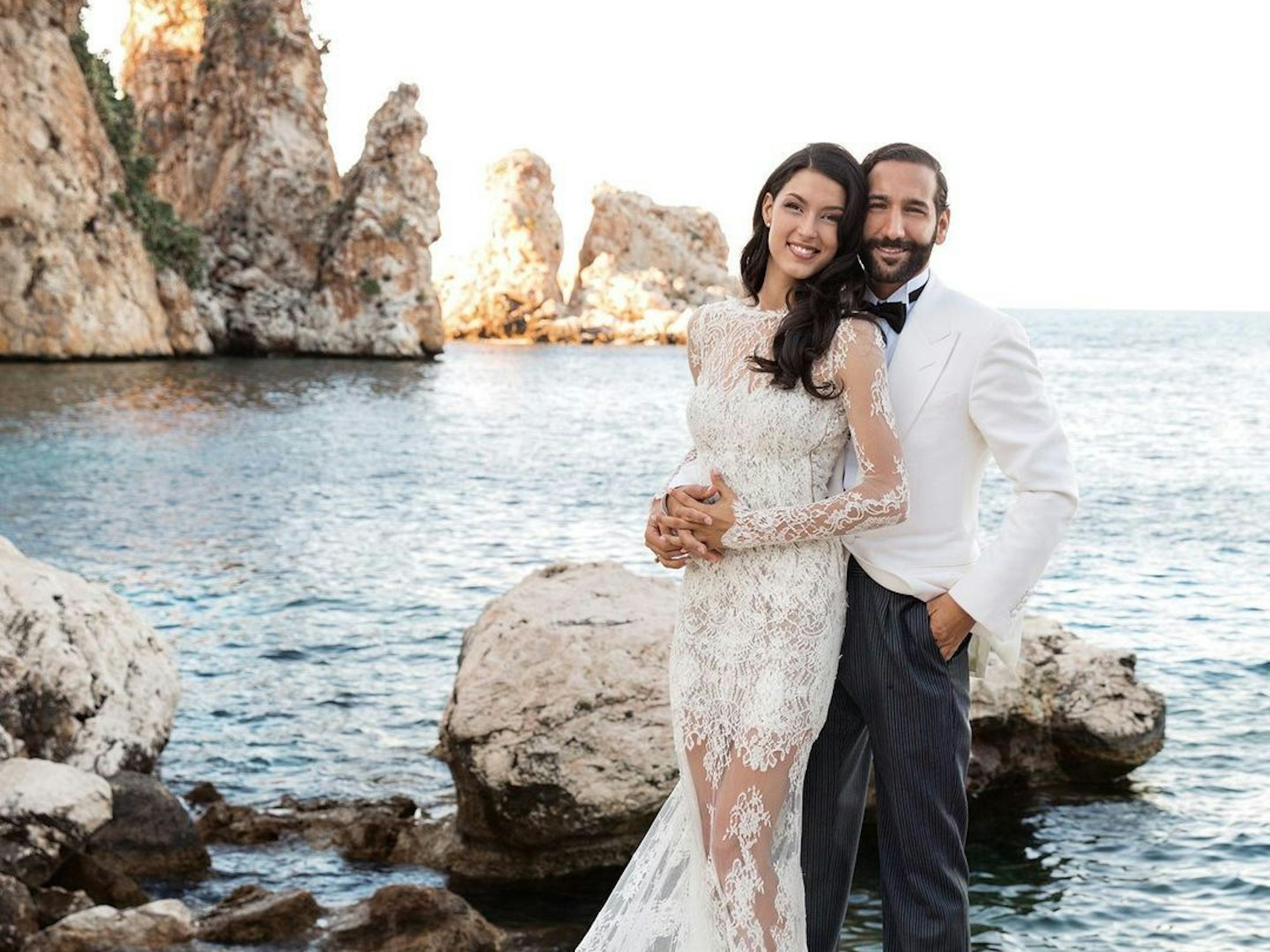 Rebecca Mir und Massimo Sinato posieren vor dem Meer.