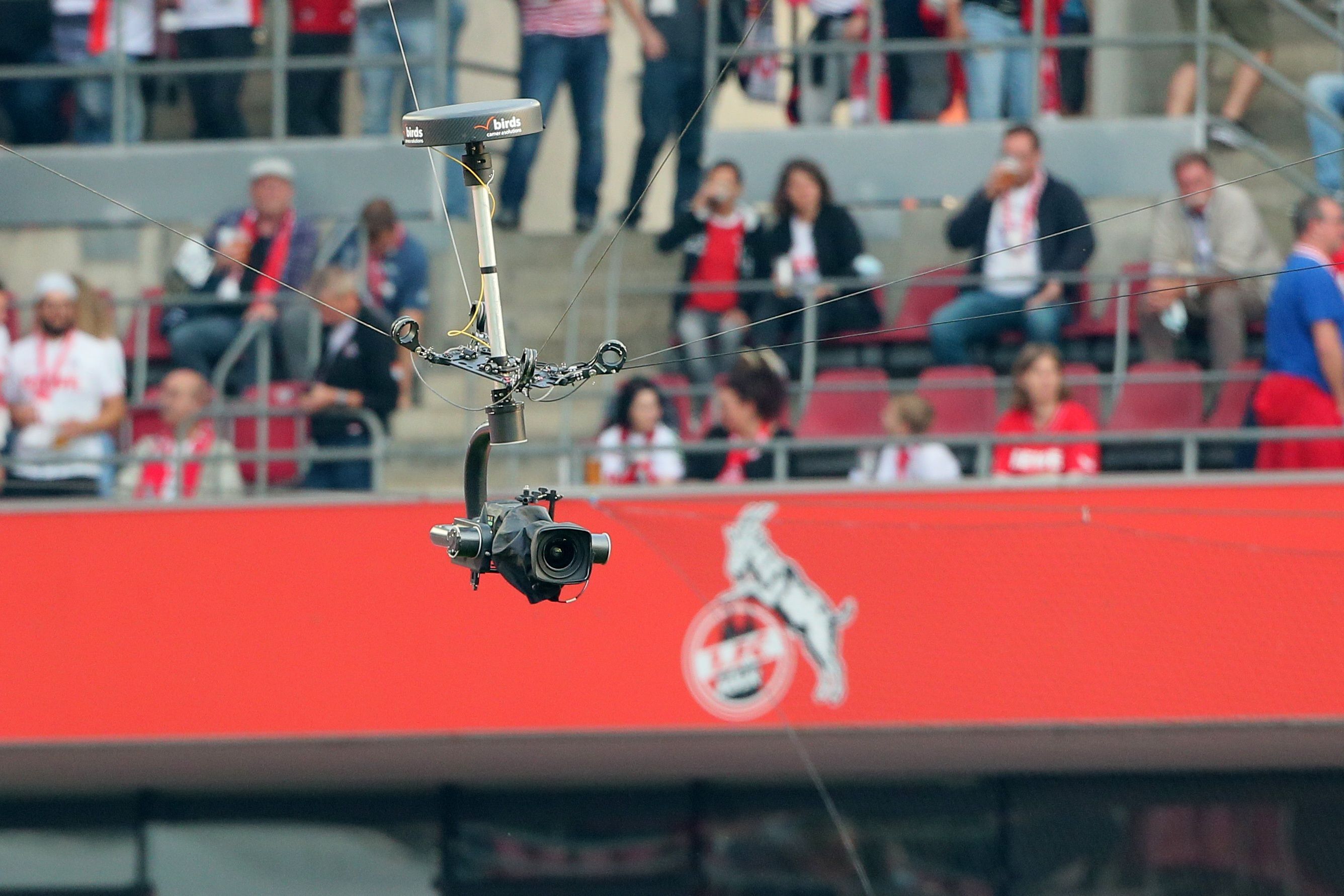 Eine Kamera schwebt im Rhein-Energie-Stadion. Im Hintergrund sind Fans und das Logo des 1. FC Köln zu erkennen.