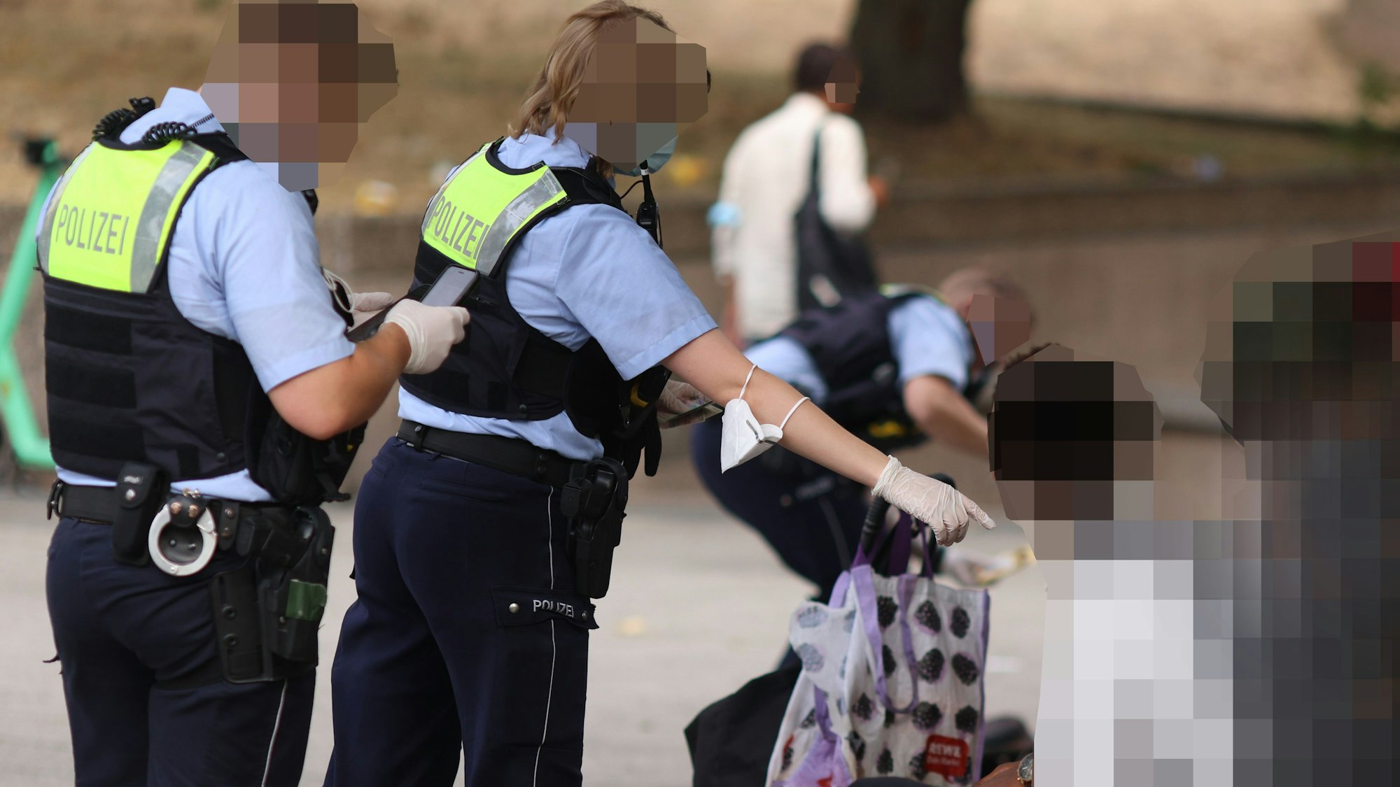 Drei Kräfte der Polizei kontrollieren Personen auf dem Ebertplatz.