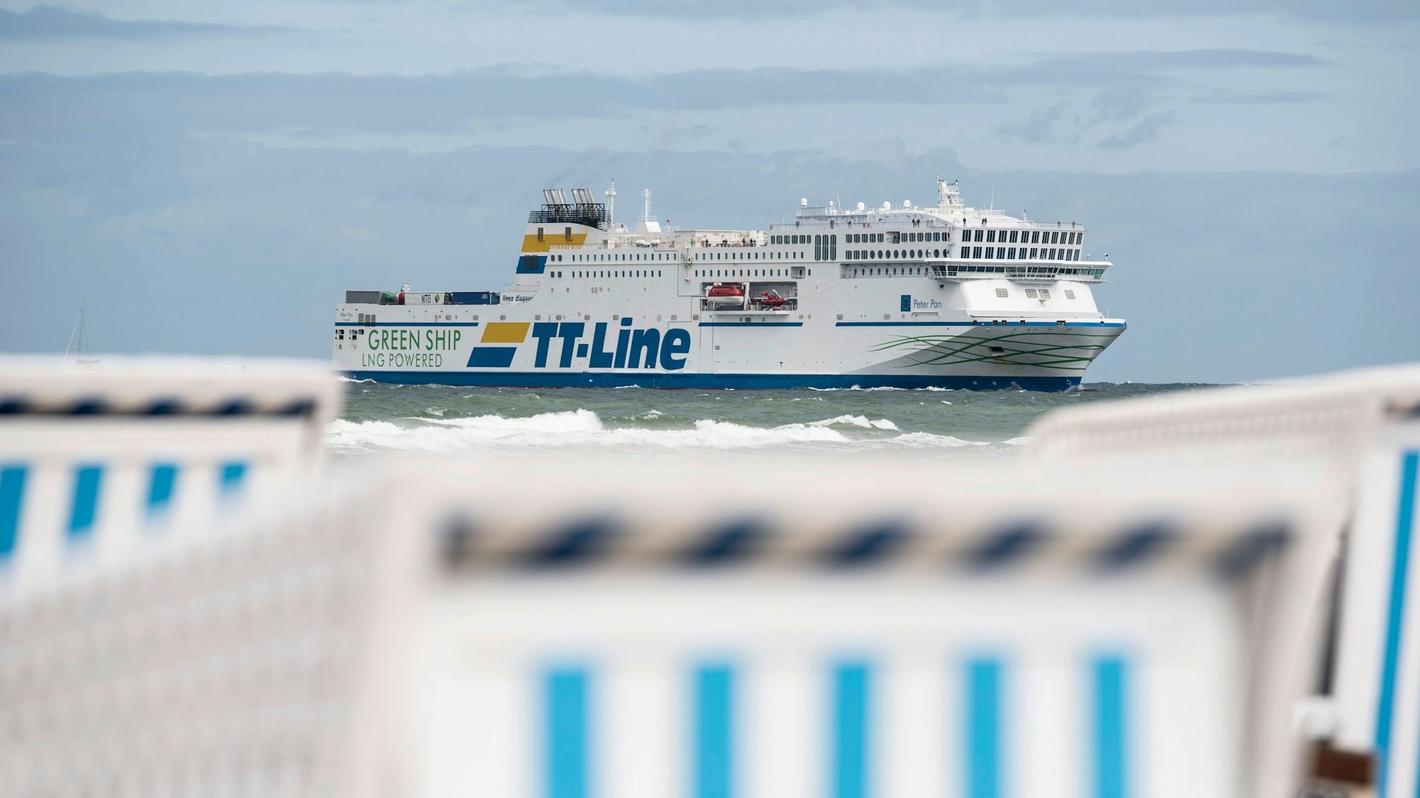 Strandkörbe stehen am Ostseestrand in Warnemünde, dahinter fährt eine Fähre der TT-Line.