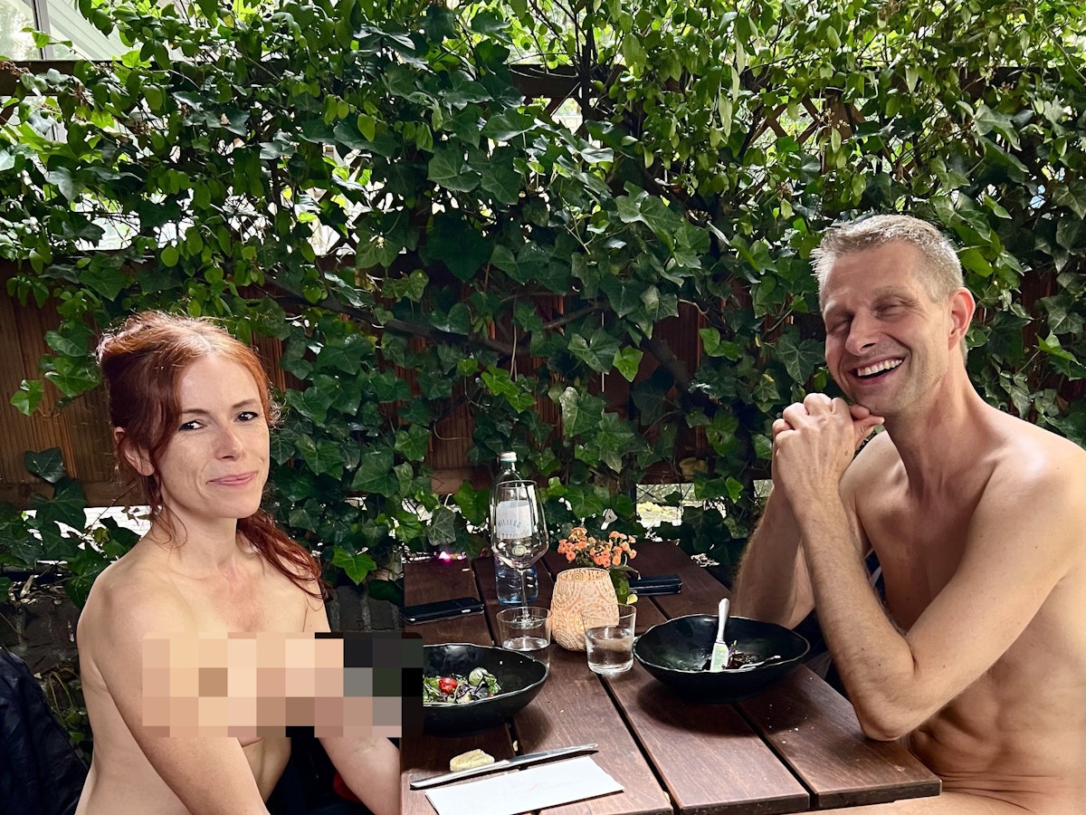 Ein nackter Mann sitzt zusammen mit einer nackten Frau in Köln an einem Restaurant-Tisch.