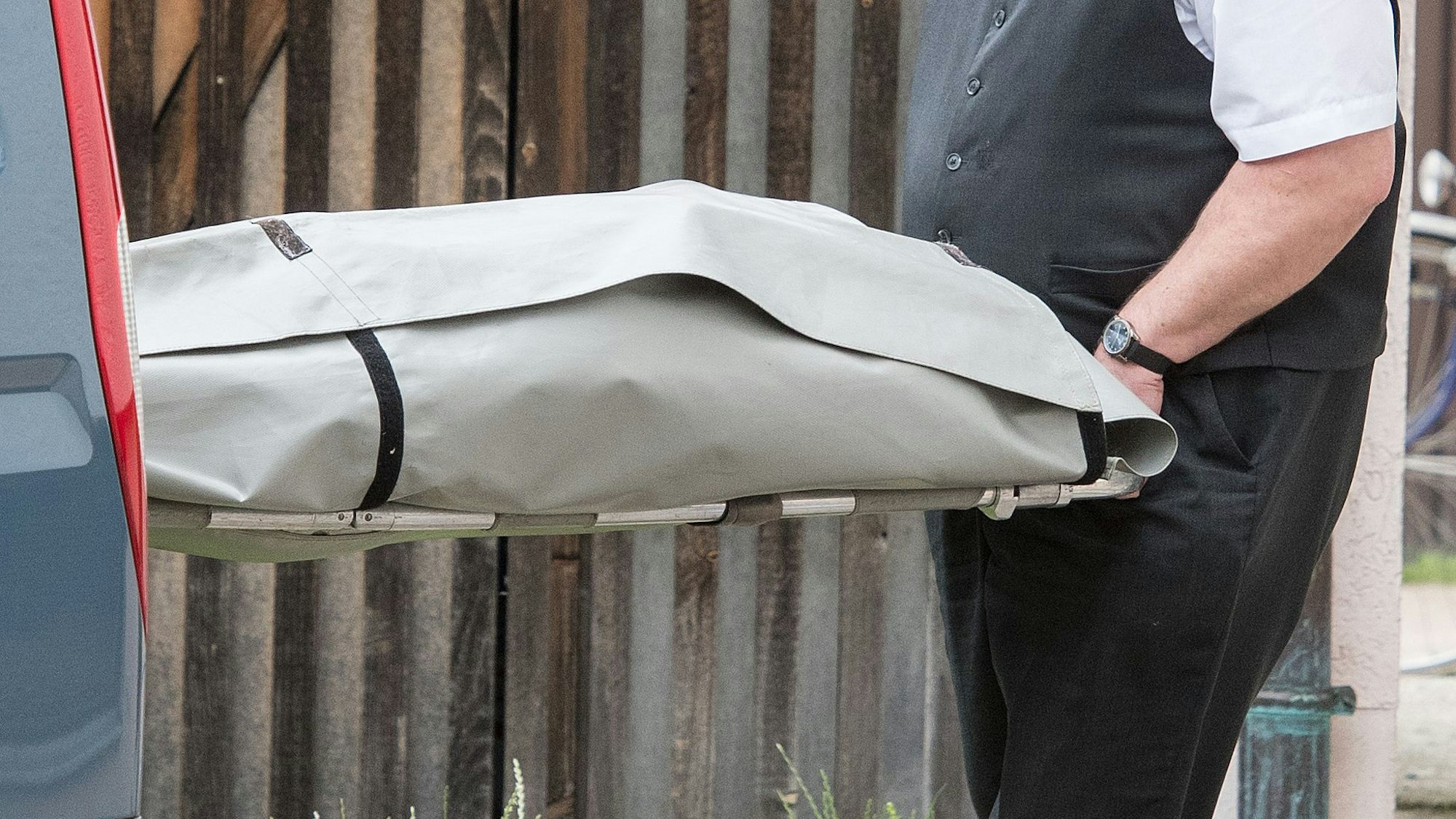 Ein Bestatter schiebt eine Person in einem Leichensack in einen Leichenwagen.