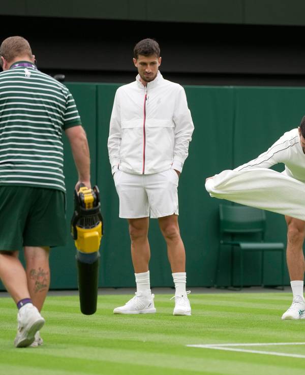 Novak Djokovic versucht, den Rasen auf dem Centre Court mit einem Handtuch-Wirbel zu trocknen.