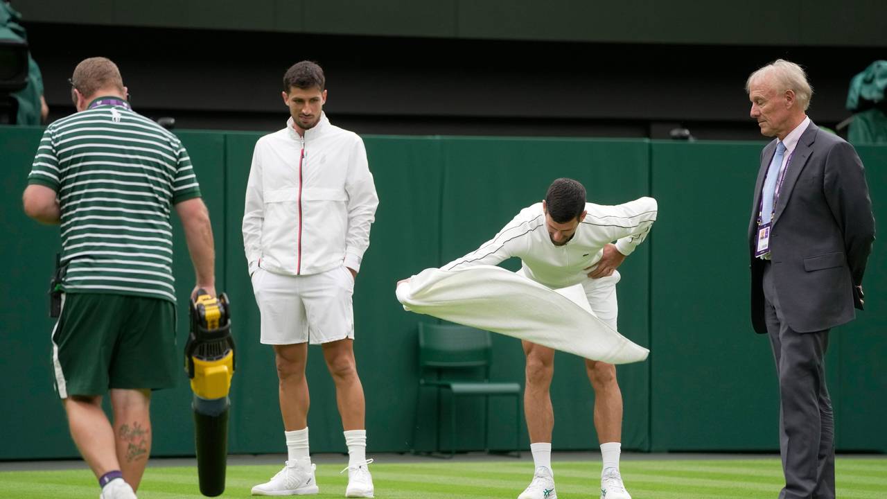 Novak Djokovic versucht, den Rasen auf dem Centre Court mit einem Handtuch-Wirbel zu trocknen.