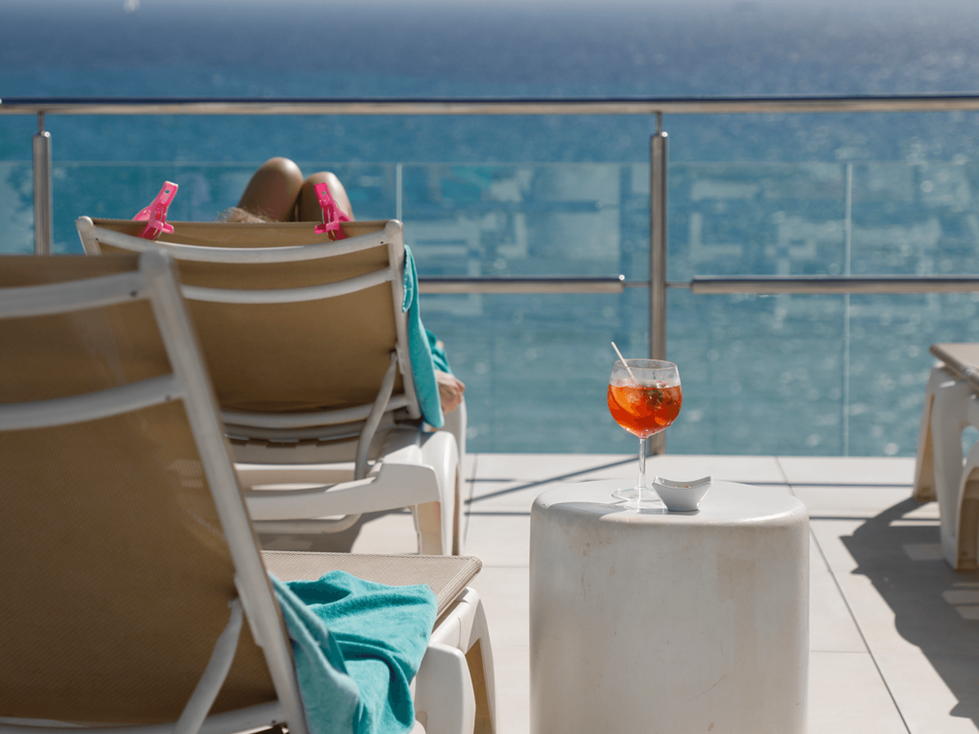 Eine Frau sonnt sich auf einer Liege. Neben ihr steht ein Aperol Spritz.