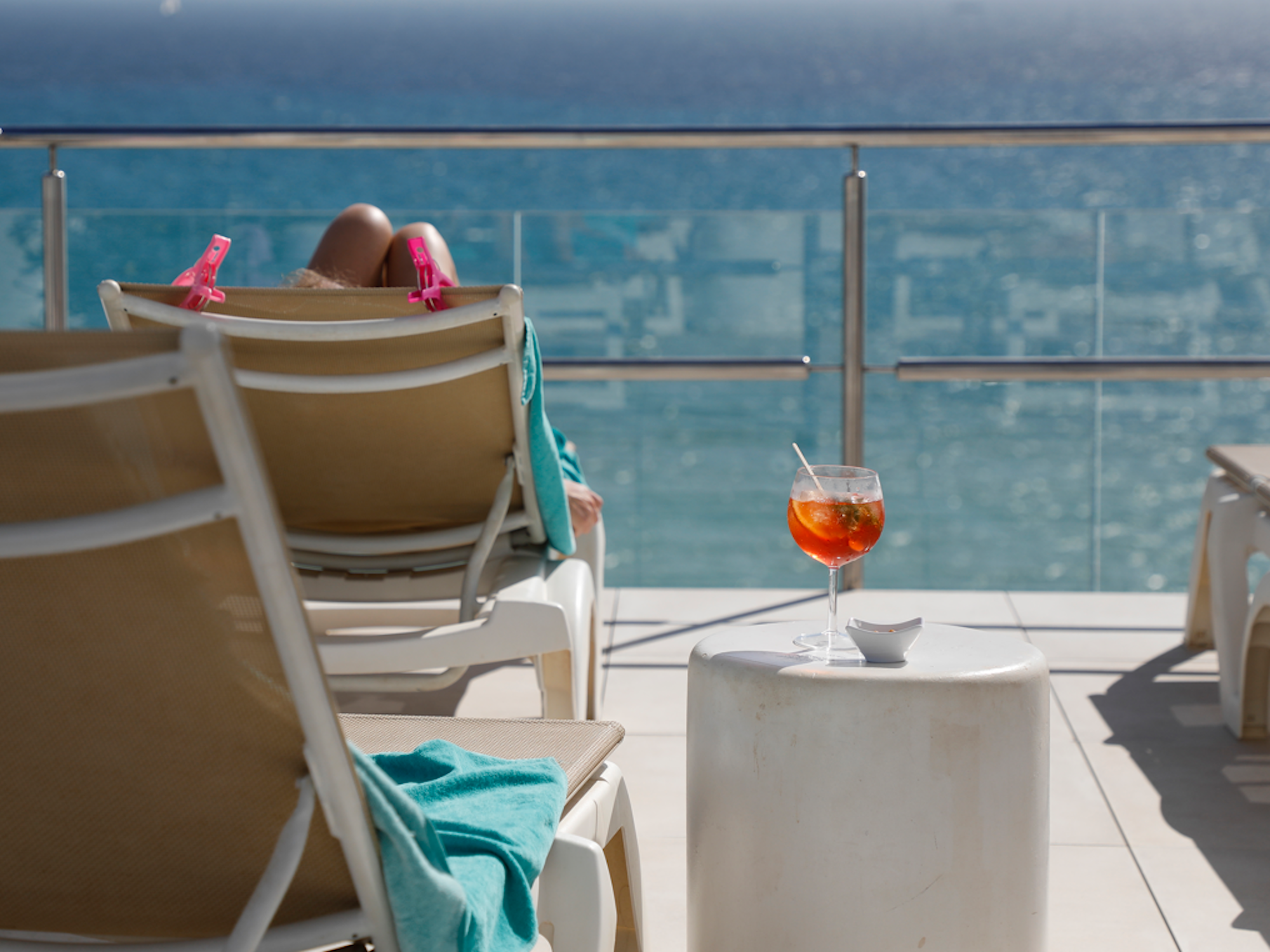 Eine Frau sonnt sich auf einer Liege. Neben ihr steht ein Aperol Spritz.