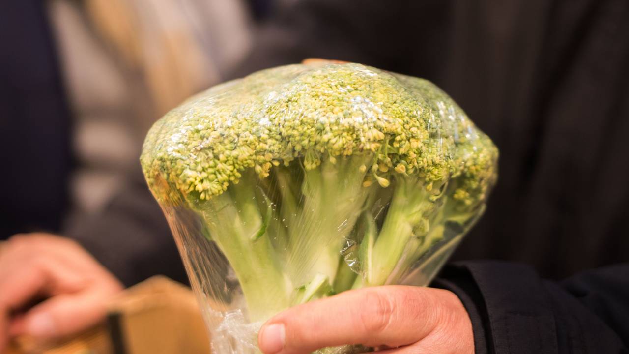 Ein Mann hält einen eingeschweißten Brokkoli in der Hand.