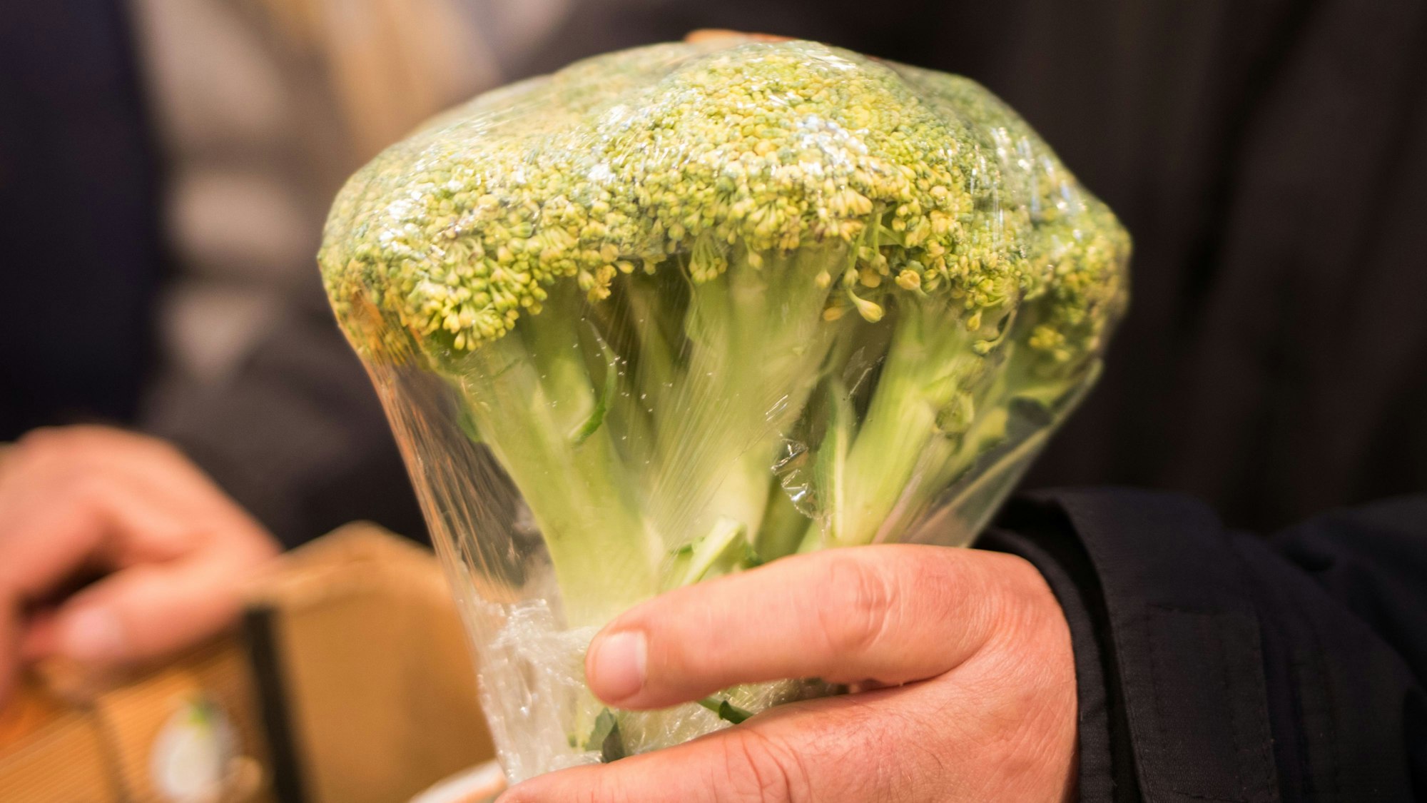 Ein Mann hält einen eingeschweißten Brokkoli in der Hand.