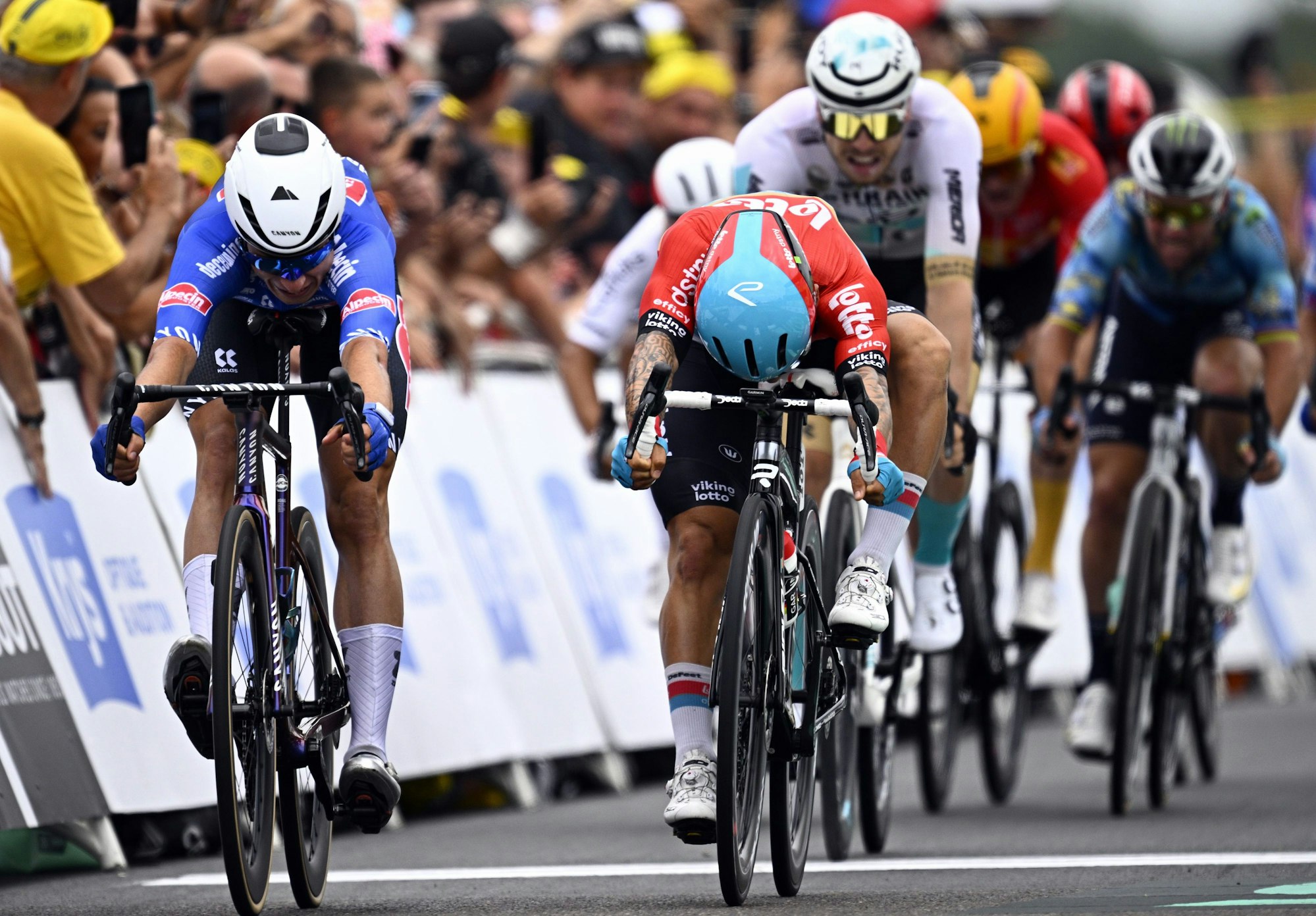 Jasper Philipsen (l) aus Belgien vom Team Alpecin-Deceuninck sprintet vor Caleb Ewan (M) aus Australien vom Team Lotto Dstny und Phil Bauhaus (Mitte r) aus Deutschland vom Team Bahrain Victorious über die Ziellinie.