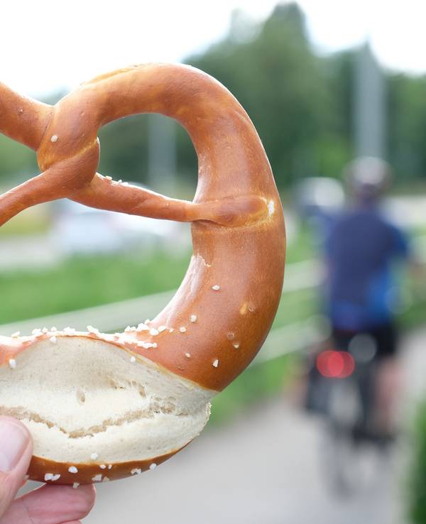 Eine Hand hält eine Brezel an einem Radweg (gestellte Szene).