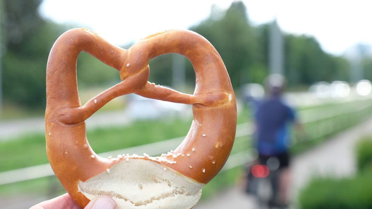 Eine Hand hält eine Brezel an einem Radweg (gestellte Szene).