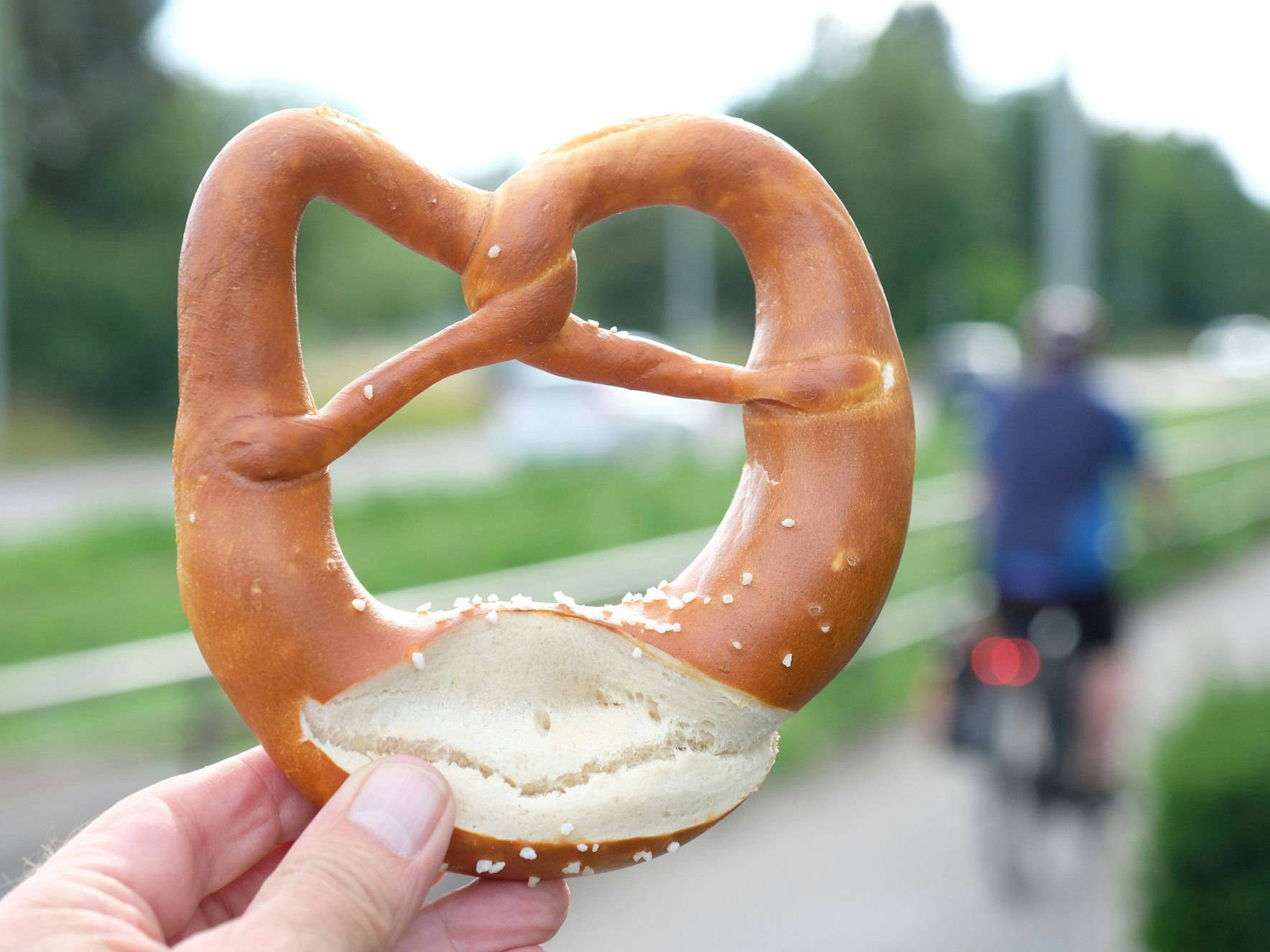 Eine Hand hält eine Brezel an einem Radweg (gestellte Szene).