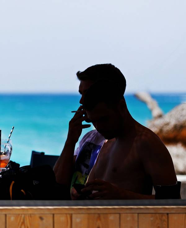 Junge Männer sitzen an der Strandpromenade am Strand von Arenal auf Mallorca in einer Bar und trinken und rauchen.