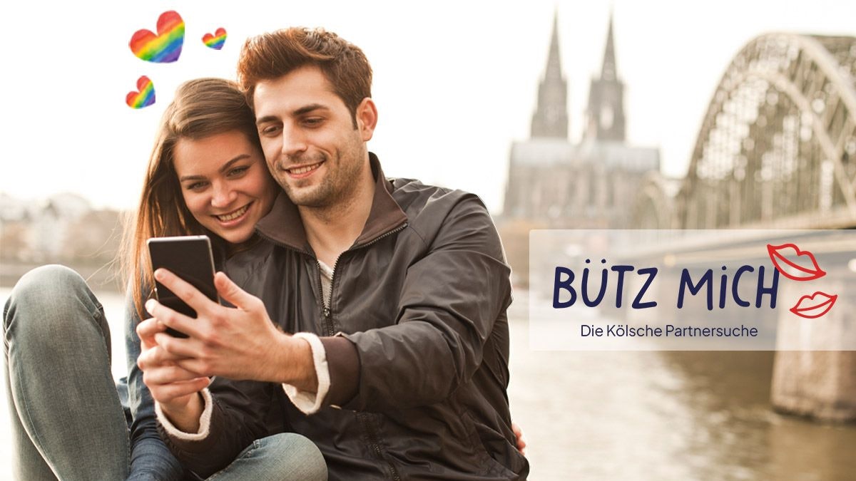 Eine Frau und ein Mann stehen auf der Rheinpromenade mit dem Kölner Dom und der Hohenzollernbrücke im Hintergrund und schauen lächelnd auf ein Smartphone. Daneben das Logo der Website Bütz mich.