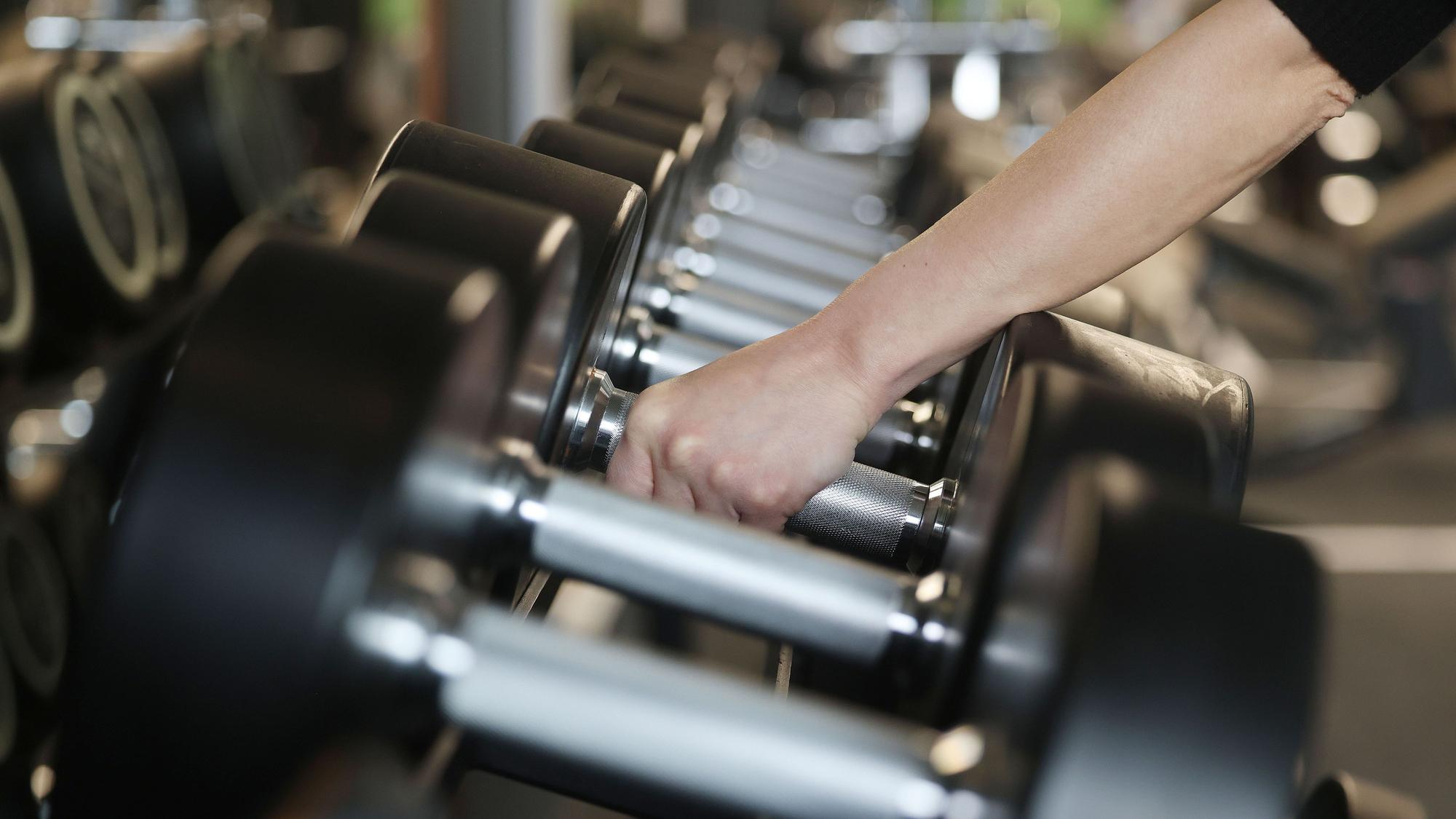 Ein Mensch greift Hanteln in einem Fitnessstudio.