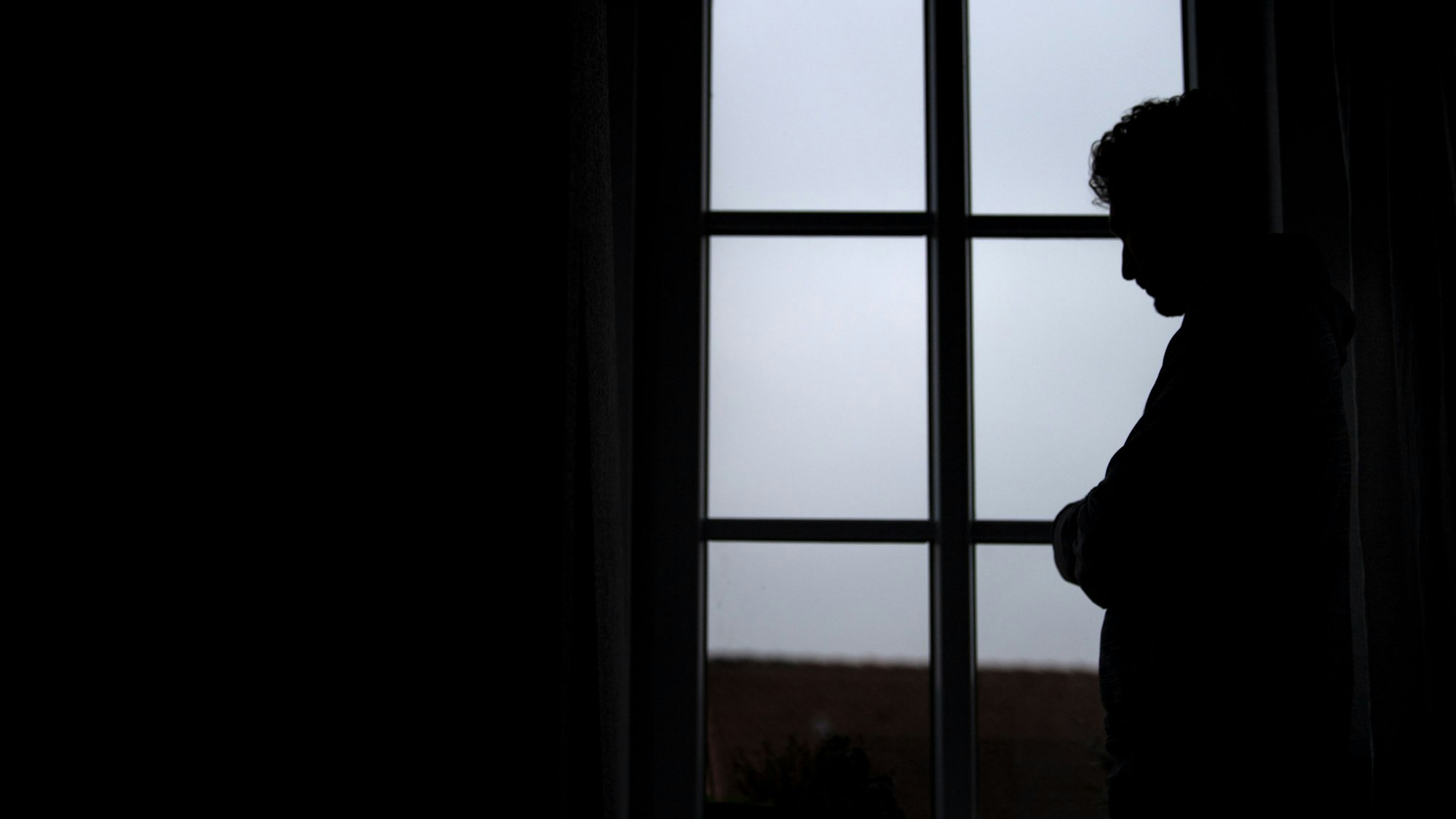 Ein Mann steht am Fenster seiner Wohnung.