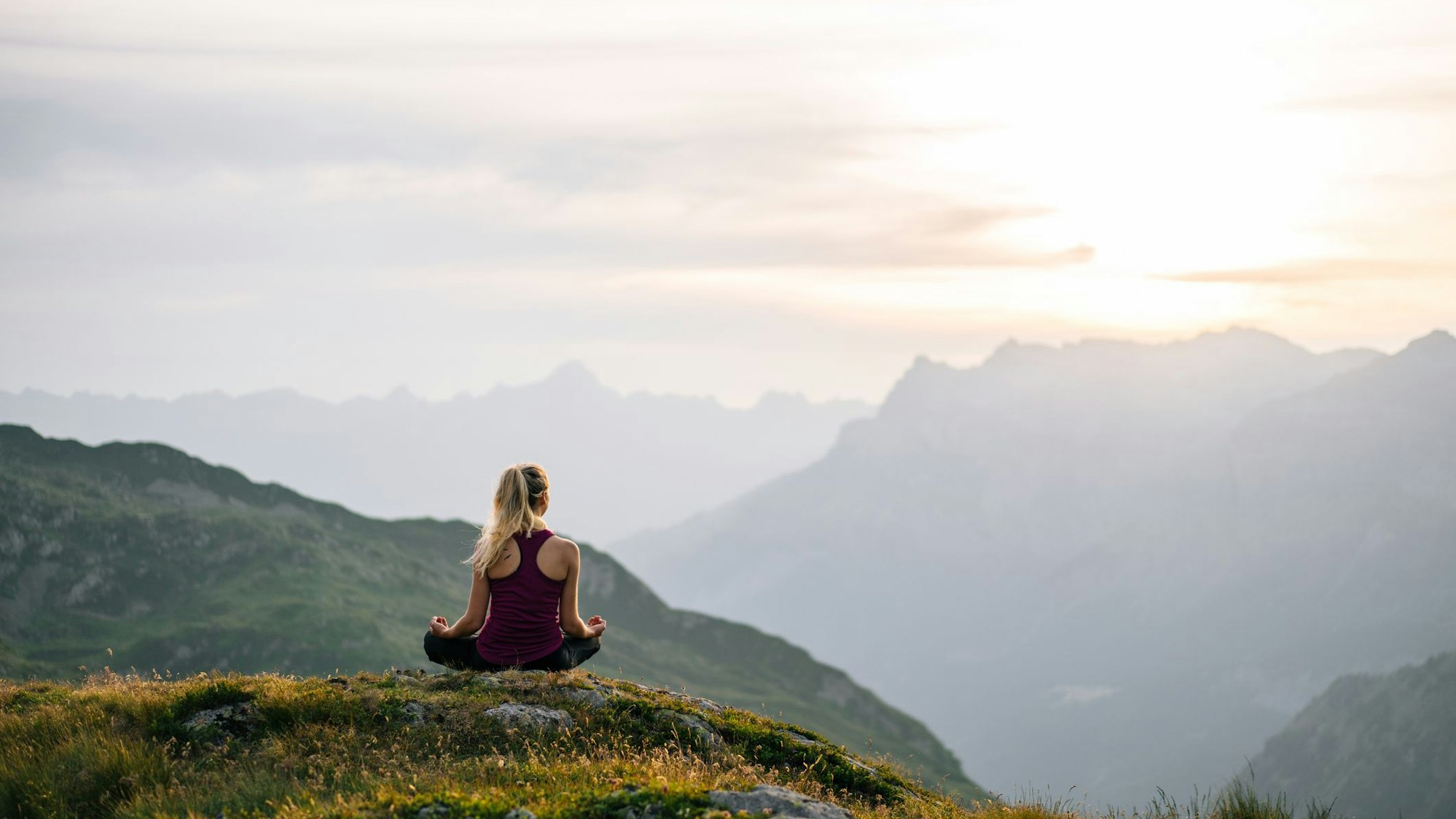 Eine Frau sitzt im Yogasitz auf einem Berg und meditiert.