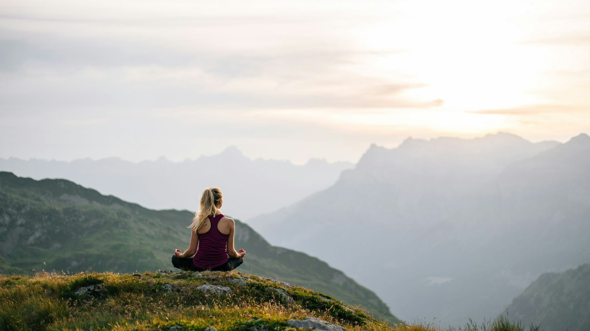 Eine Frau sitzt im Yogasitz auf einem Berg und meditiert.