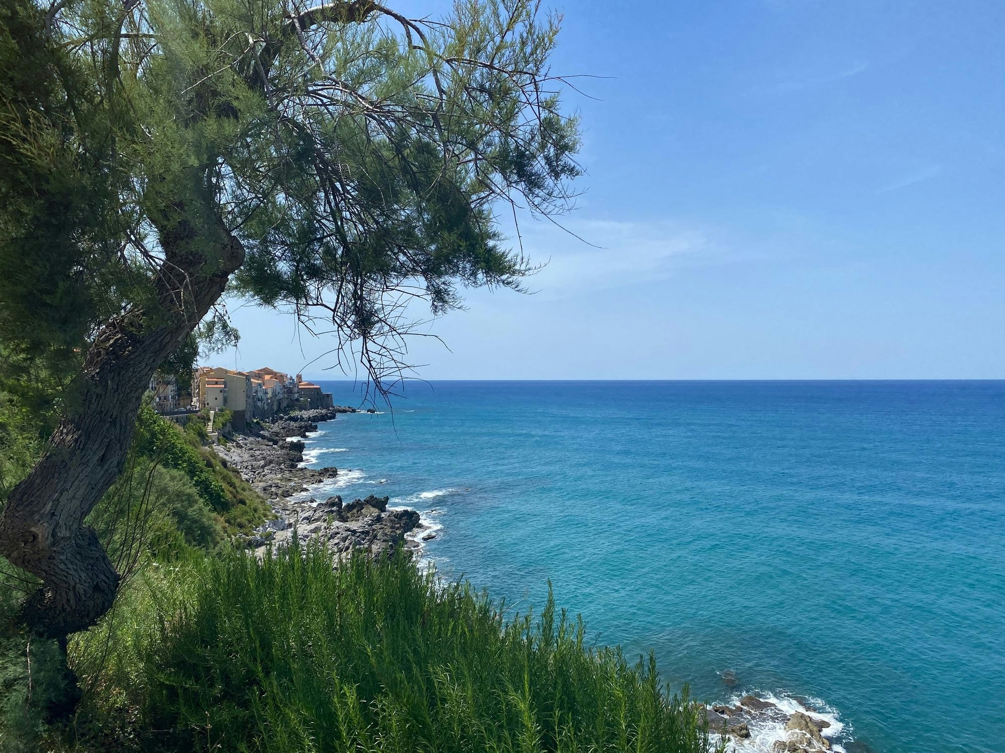 Der Blick von einer Klippe auf das offene Meer. Links auf der Klippe sind Häuser zu sehen.