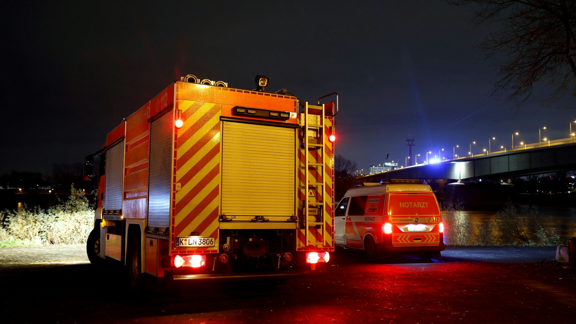 Ein Löschfahrzeug und ein zweites Einsatzfahrzeug stehen in der Nacht unterhalb einer Brücke.