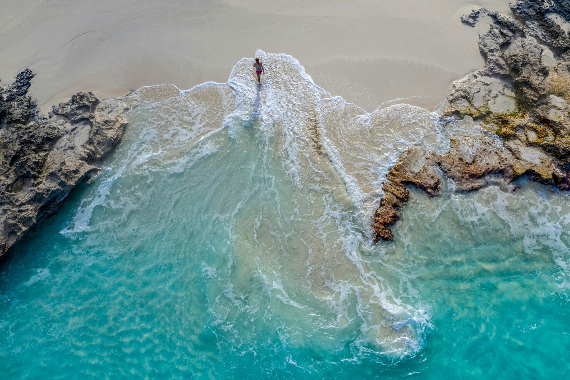 Eine Frau, die am Strand entlang geht. Die Bucht wurde von oben fotografiert.