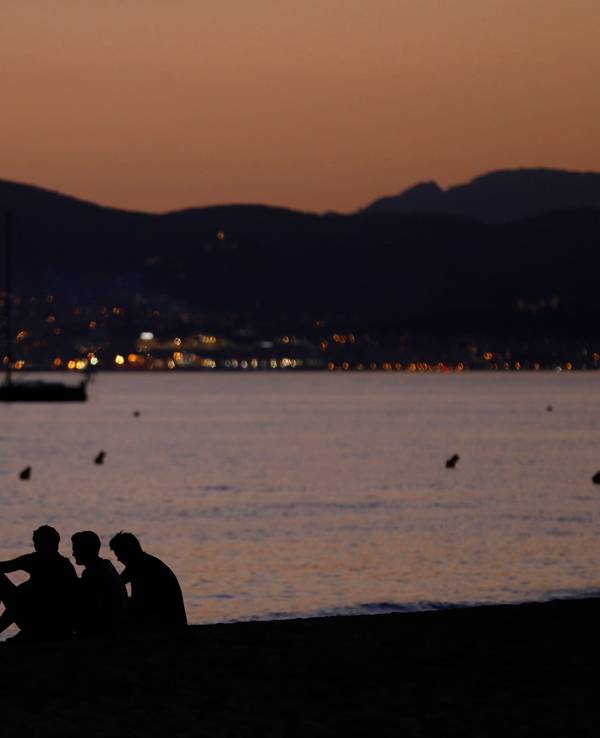 Vier Personen sitzen nach Sonnenuntergang am Strand von Palma de Mallorca.
