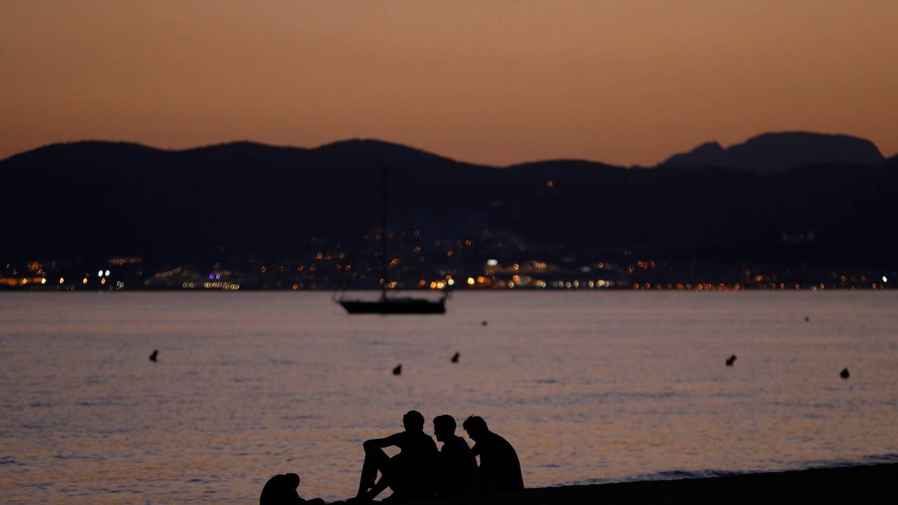 Vier Personen sitzen nach Sonnenuntergang am Strand von Palma de Mallorca.