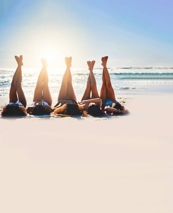 Junge Frauen am Strand strecken ihre Beine in die Höhe.