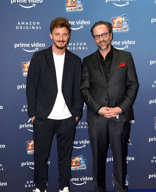 Tommi Schmitt und Kurt Krömer posieren vor einer Werbewand und schauen in die Kamera.