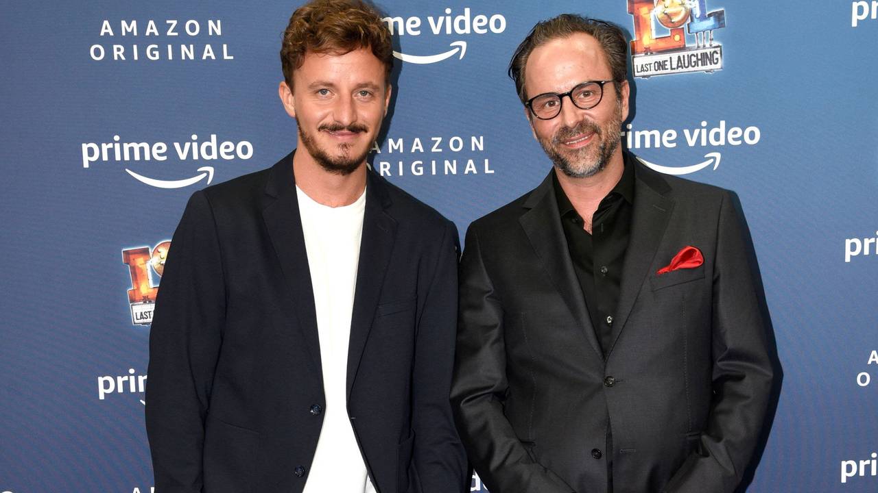 Tommi Schmitt und Kurt Krömer posieren vor einer Werbewand und schauen in die Kamera.