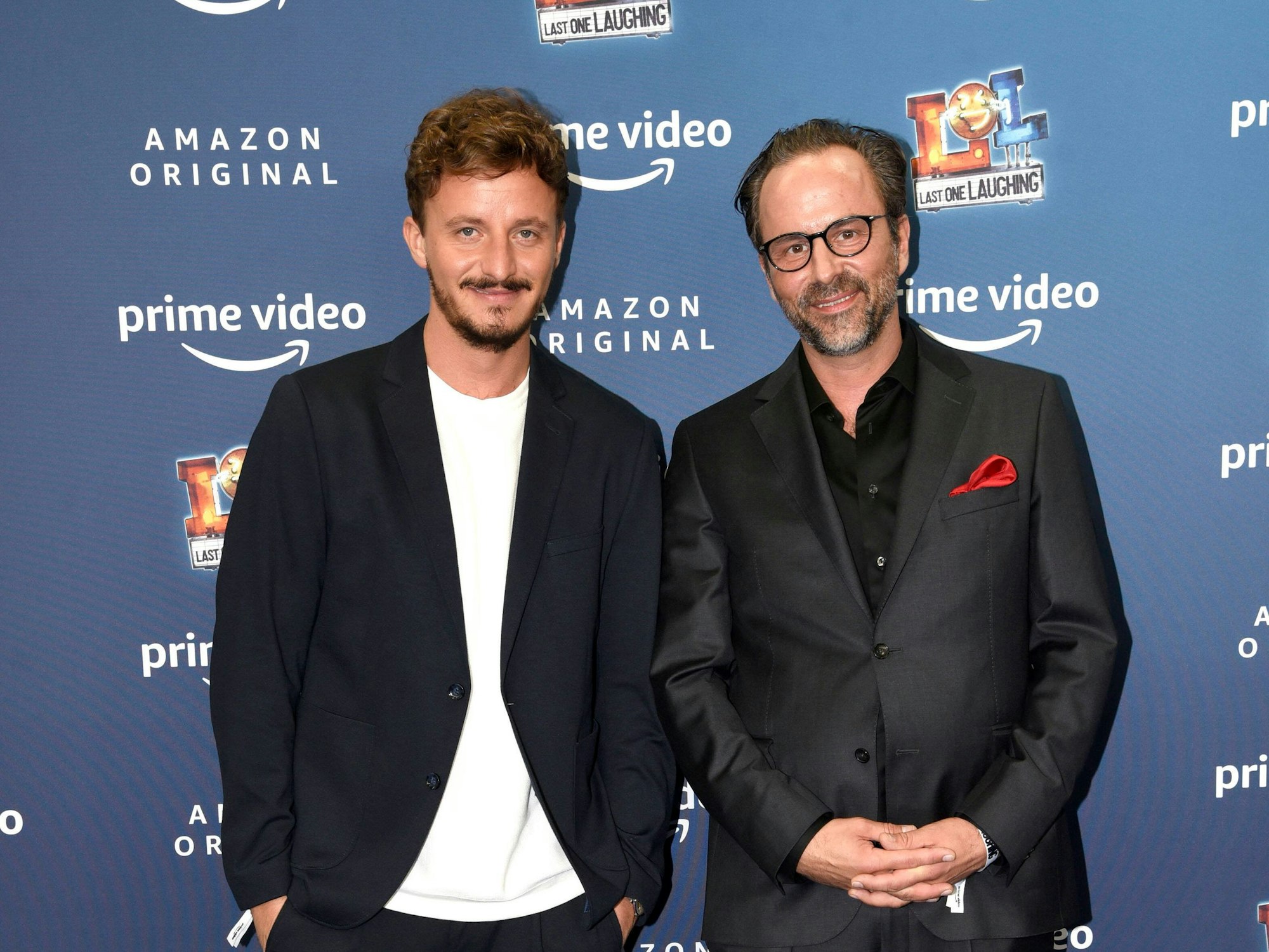 Tommi Schmitt und Kurt Krömer posieren vor einer Werbewand und schauen in die Kamera.