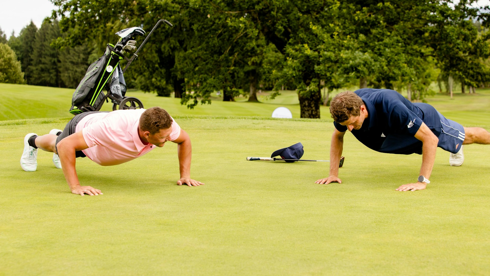 Thomas Müller (r.) und Thomas Dreßen machen beim Benefiz-Turnier der Nicolaidis YoungWings Stiftung Liegestütze auf dem Golfplatz.
