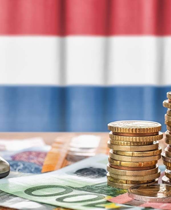 Euro Banknoten und Münzen liegen vor der niederländischen Flagge.