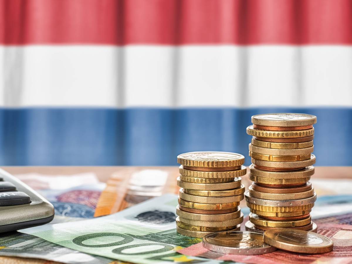 Euro Banknoten und Münzen liegen vor der niederländischen Flagge.