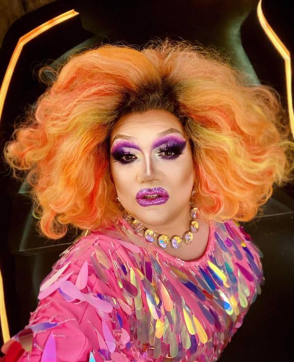 Die Dragqueen Electra Pain in pinken Glitzeroutfit und einer orangen Perücke.