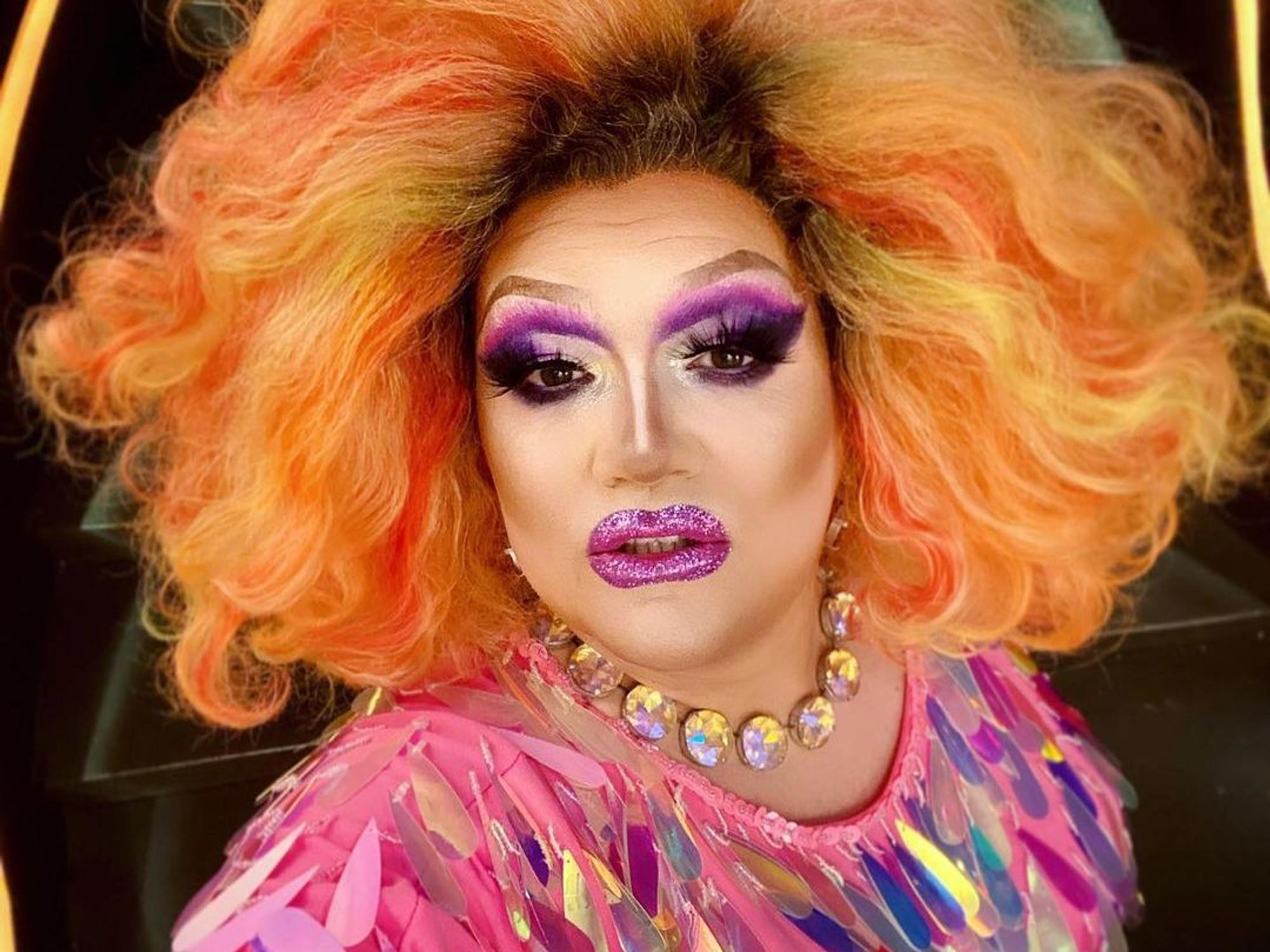 Die Dragqueen Electra Pain in pinken Glitzeroutfit und einer orangen Perücke.