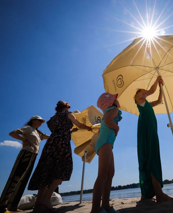 Vier Personen spannen zwei Sonnenschirme am See auf.