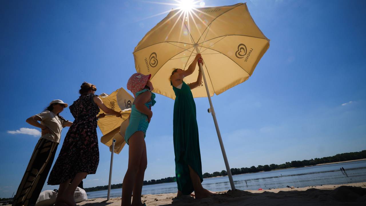 Vier Personen spannen zwei Sonnenschirme am See auf.