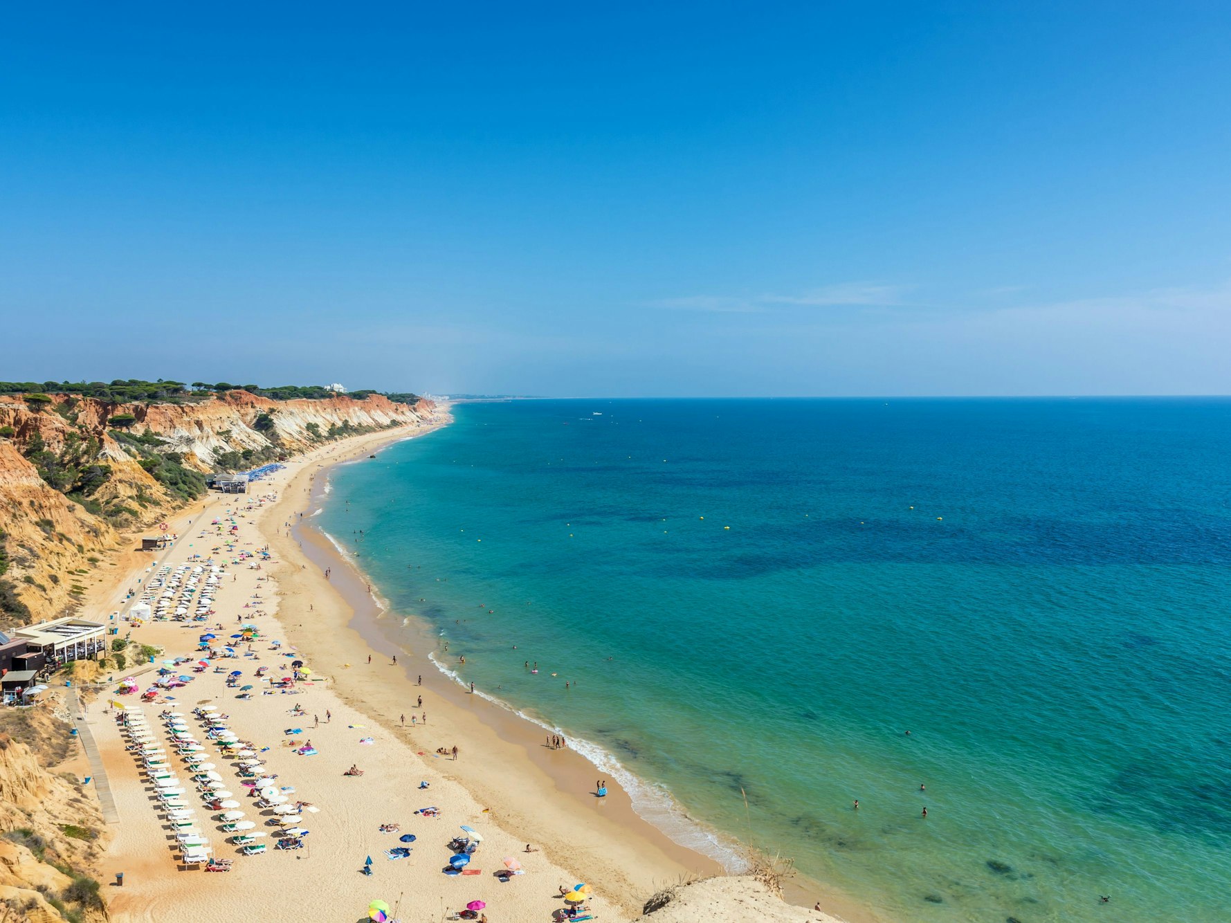Sonnenliegen sowie Urlauberinnen und Urlauber in der Fig Tree Bay (Feigenbaumbucht) von Protaras auf Zypern. Sonnenliegen und Badegäste an der Praia da Falésia in Albufeira (Portugal). Der Strand zählt zu den besten preiswerten Stränden in Europa.