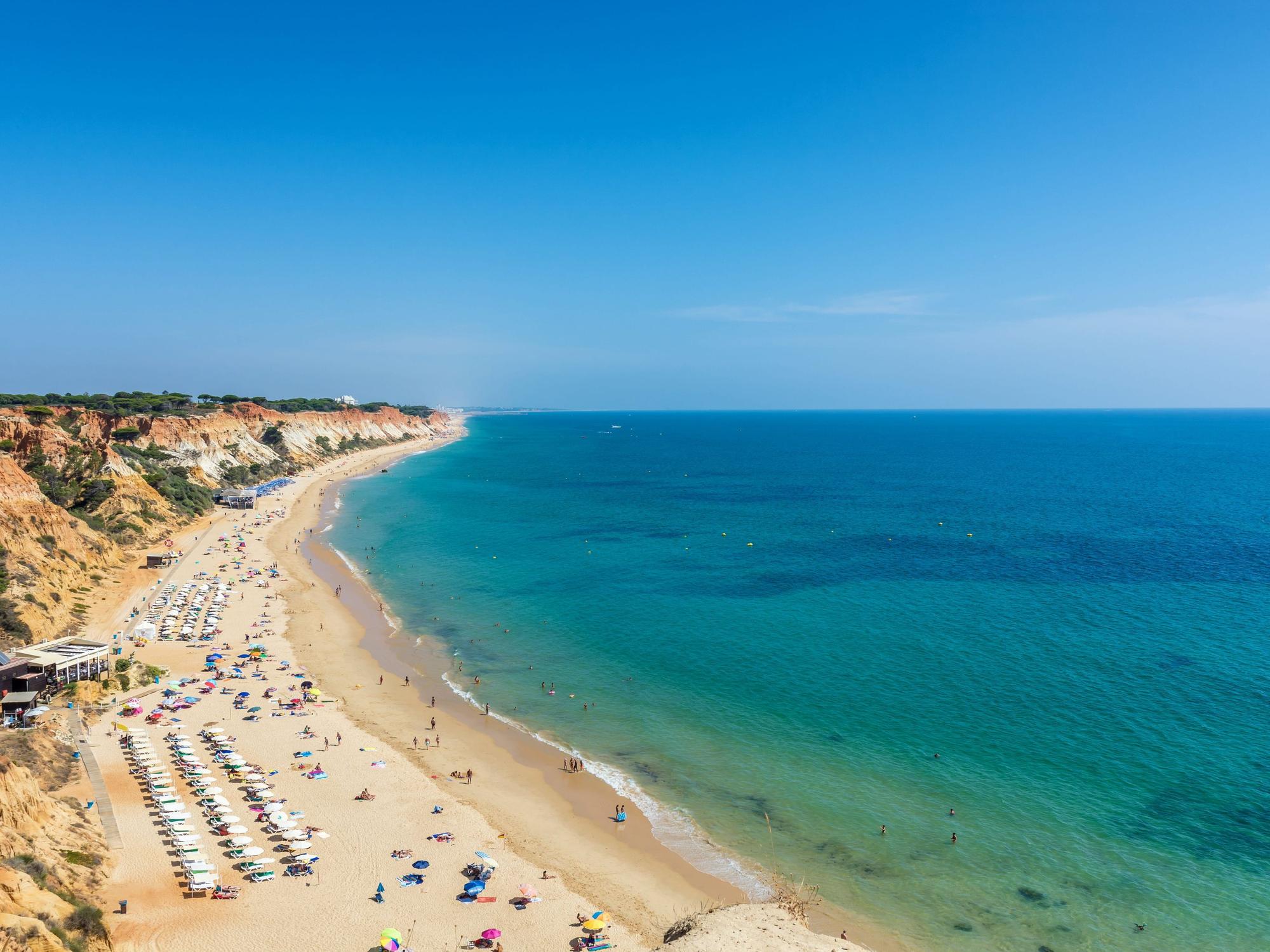 Sonnenliegen sowie Urlauberinnen und Urlauber in der Fig Tree Bay (Feigenbaumbucht) von Protaras auf Zypern. Sonnenliegen und Badegäste an der Praia da Falésia in Albufeira (Portugal). Der Strand zählt zu den besten preiswerten Stränden in Europa.