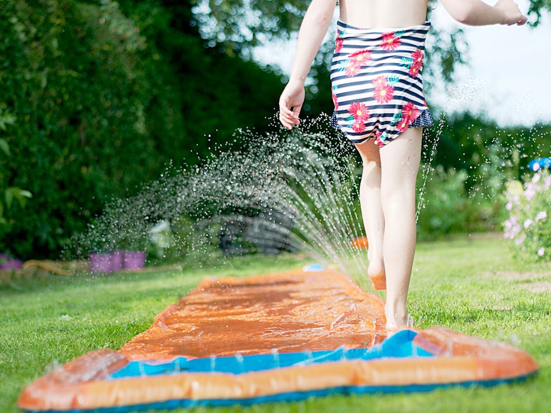 Ein Mädchen spielt mit einer Wasserrutsche im Garten.