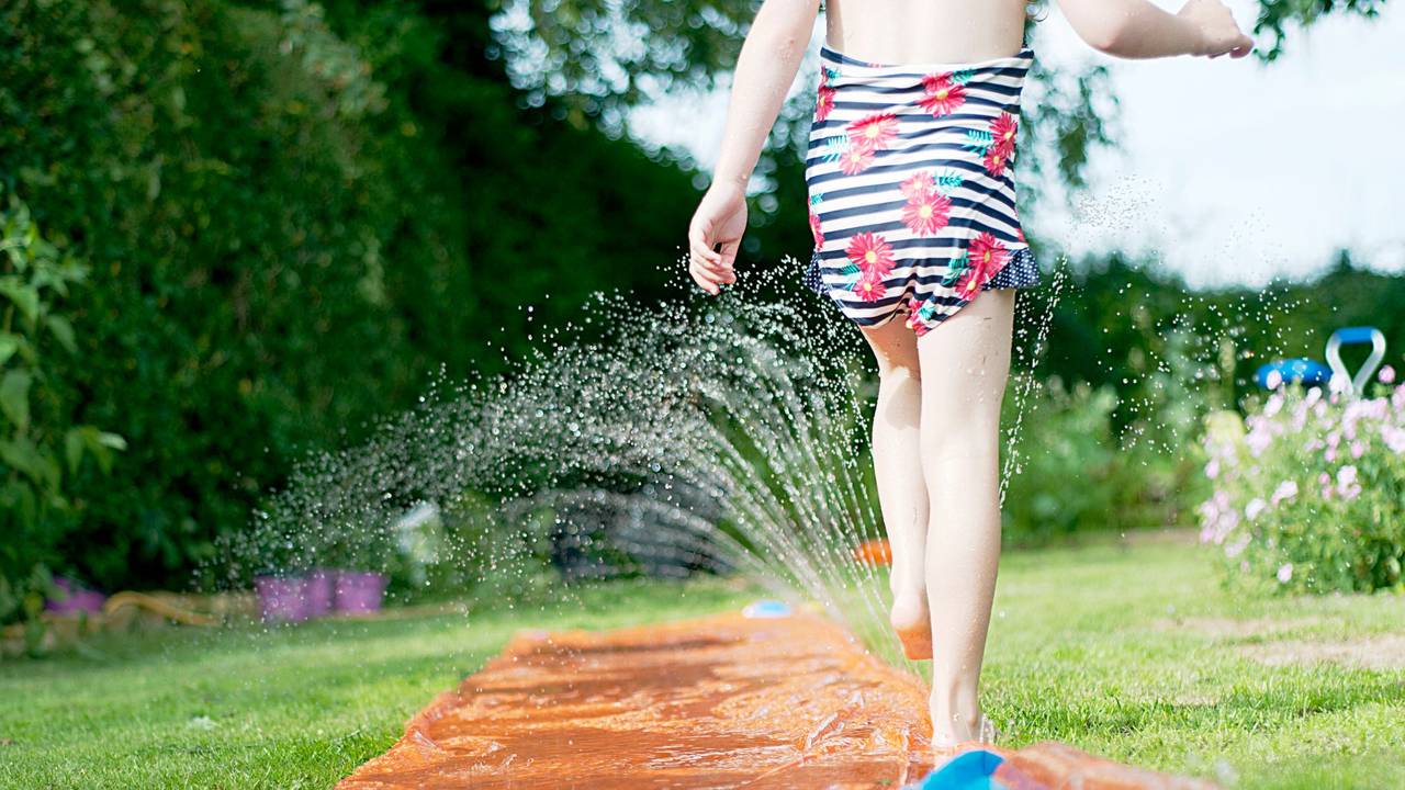 Ein Mädchen spielt mit einer Wasserrutsche im Garten.