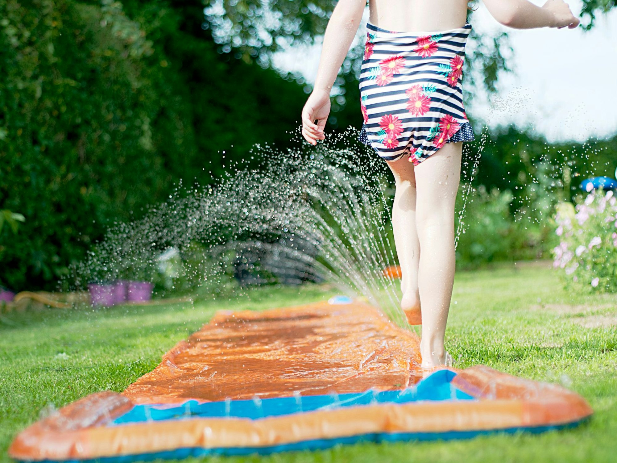 Ein Mädchen spielt mit einer Wasserrutsche im Garten.