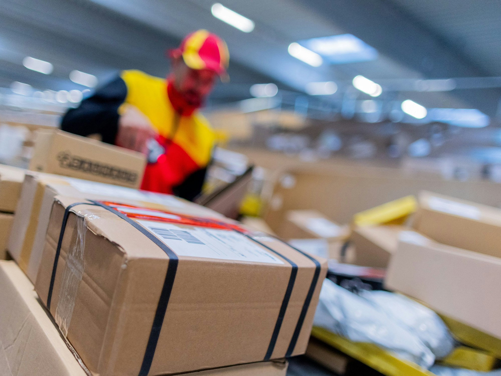 Ein Paketzusteller sortiert und räumt in einer Zustellbasis von Deutsche Post DHL Pakete in ein Zustellfahrzeug.